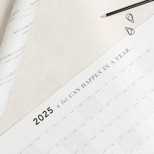 A close up of the title of the A1 A Lot Can Happen In A Year Wall Planner. Next to it is a planner that has been rolled and wrapped in tissue paper.