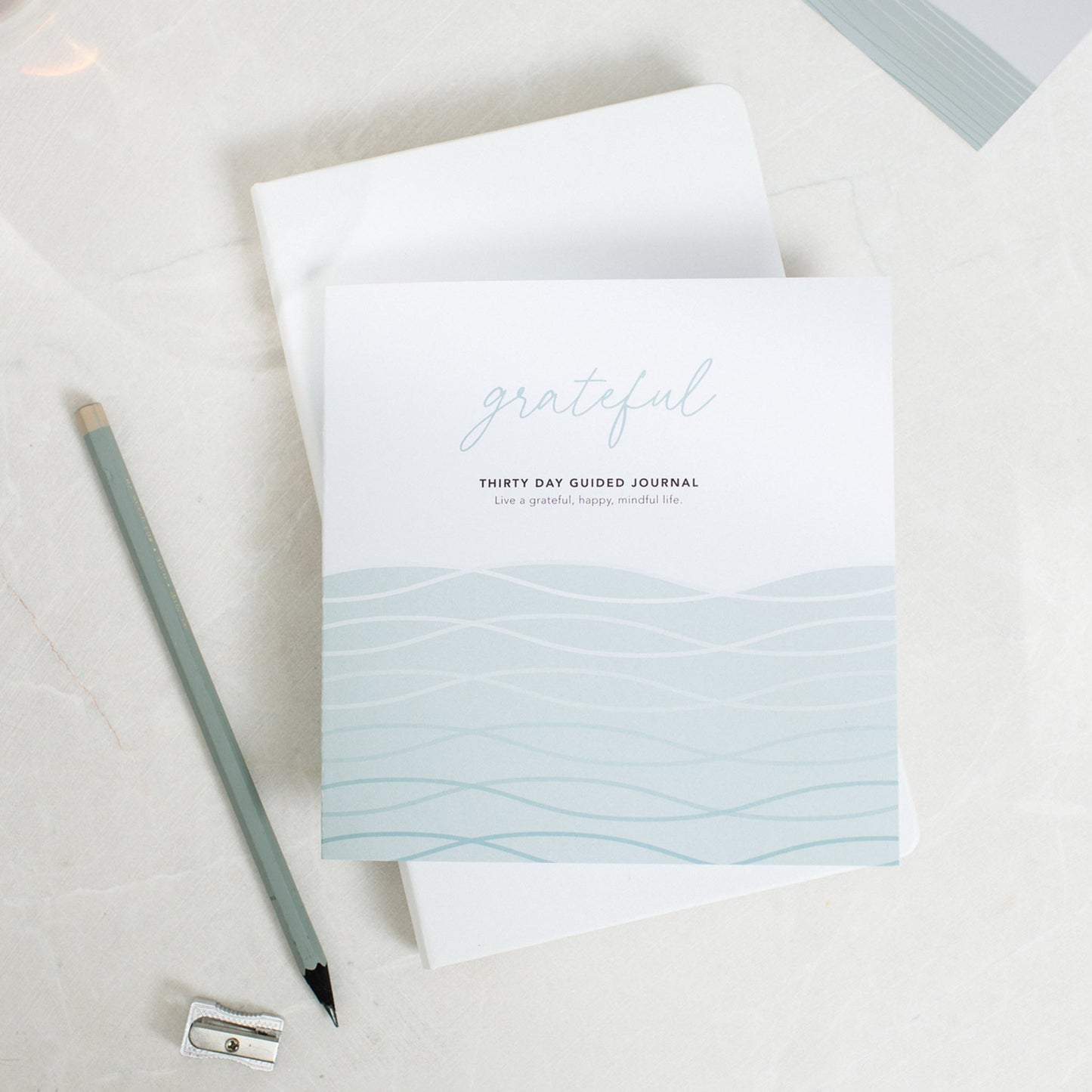 Grateful guided gratitude journal, placed on top of another journal with a pencil and pencil sharpener next to it