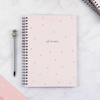 The cover of the pink polka dot IVF Planner with a pineapple pen next to it.